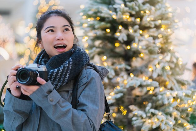 Happiness beautiful asian female hand hold camera enjoy christmas tree with lighting decorate and golden blur bokeh background