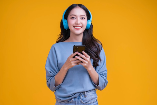 ヘッドフォンスマートフォンを身に着けている幸せのんきなアジアの若い女性の女性ティーンは音楽を聞く楽しい楽しい動く瞬間ティーンは笑いながらカサウルスの布を歌う動きを歌うトレンディなライフスタイルスタジオショット