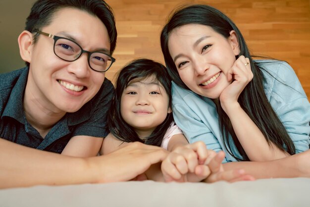 Happiness joyful asian family mom dad daughter laydown together with fun play kiss on bed portrait of asian family people home background