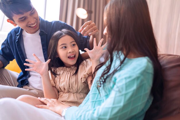 Счастье, милая азиатская семья, отец, мать и дочь, сидящие вместе на диване и смотрящие фильм по телевизору дома, смеются, улыбаясь, улыбаясь, азиатская семья дома, изоляция, карантинный момент в государственном порядке блокировки.