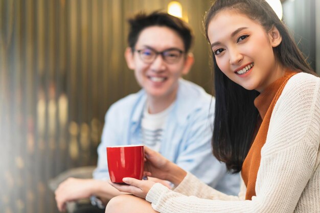 Happiness young asian couple marry family enjoy tv show and good conversation embrace together hand hold coffee drink laugh smile together on sofa couch in living room home interior background