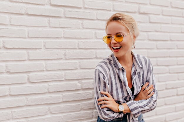 Happy adorable blond woman wearing stylish orange glasses in striped shirt posing with lovely smile
