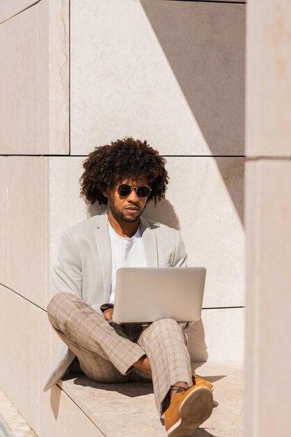 Happy African American businessman working in open air. Man in suit with beard using laptop. Sitting at terrace or rooftops. Working, manager, technology concept