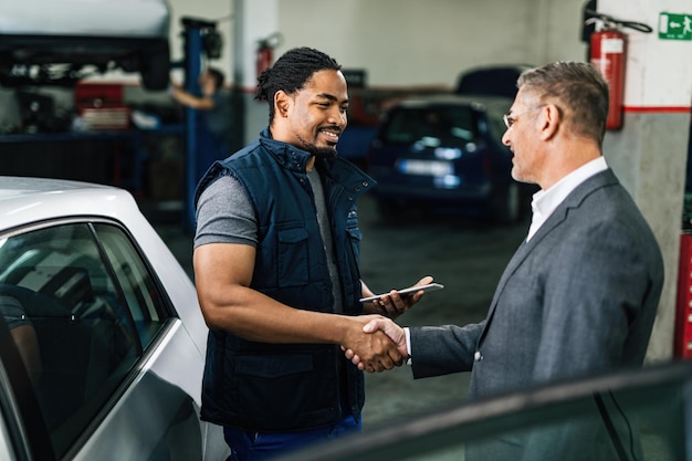 Happy African American car repairman greeting with male customer in auto repair shop