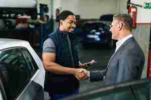 Бесплатное фото Счастливый афроамериканский авторемонтник приветствует клиента-мужчину в автомастерской