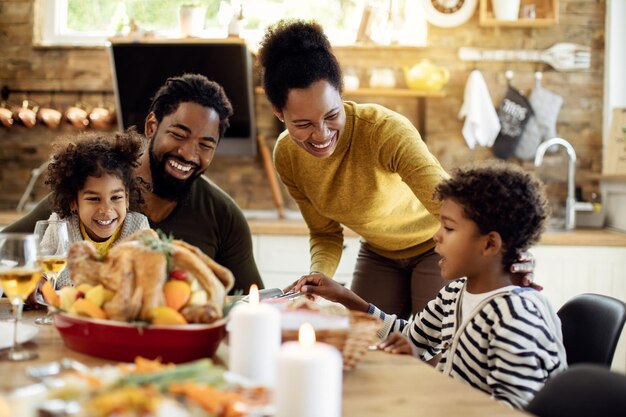 Happy African American family having fun during Thanksgiving lunch at dining table