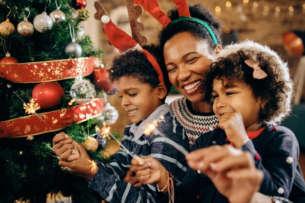 Счастливая афроамериканская семья использует бенгальские огни во время празднования Рождества дома