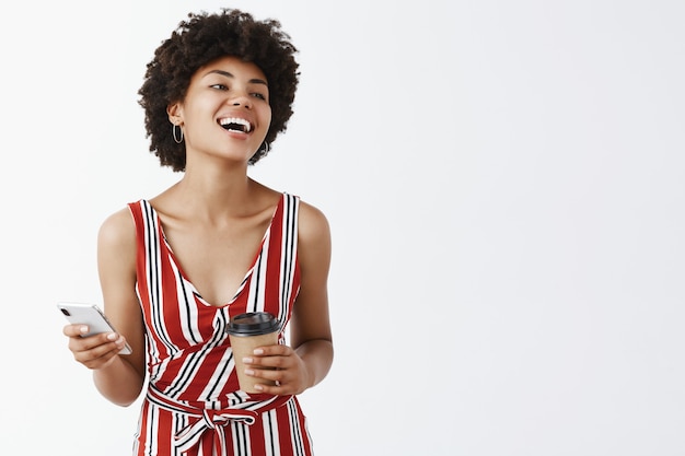 Felice afro-americano che tiene tazza di caffè e telefono, guardando a destra con gioia