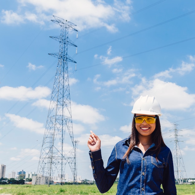 Happy African American lady in safety helmet pointing at high voltage line