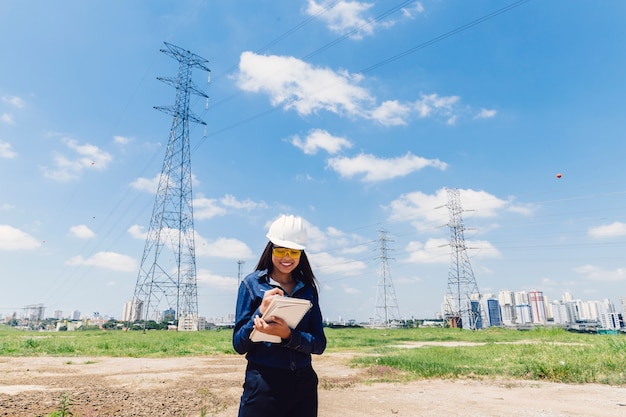 Free photo happy african american lady in safety helmet taking notes near high voltage line