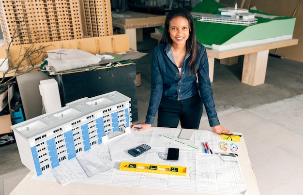 Happy African-American lady standing near model of building on table