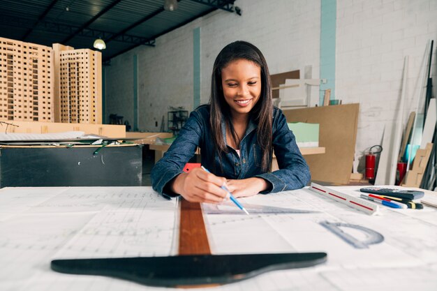 Happy African-American lady with big ruler and pen at table