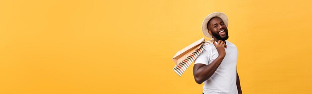 Happy african american man holding shopping bags on yellow background holidays concept