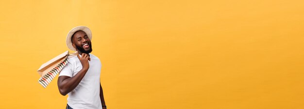 アフリカ系アメリカ人の幸せな男性が黄色い背景のホリデーコンセプトでショッピングバッグを持っています