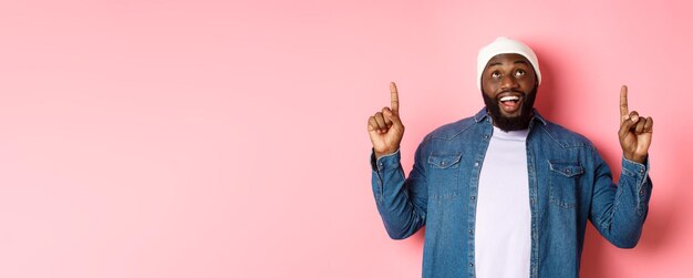 Free photo happy african american man showing advertisement smiling amazed and staring at camera pointing finge