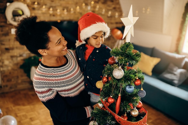 Happy African American mother and daughter by Christmas tree at home