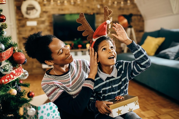 행복한 아프리카계 미국인 어머니와 아들이 크리스마스 날 집에서 즐거운 시간을 보내고 있습니다.