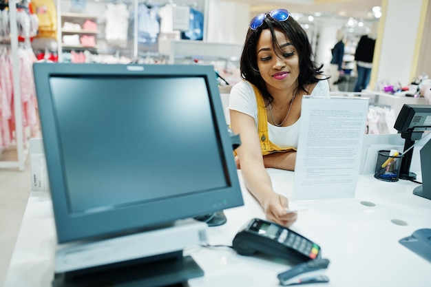 Cliente donna afroamericana felice con borse della spesa colorate che pagano con carta di credito vicino a terminali in contanti con pos