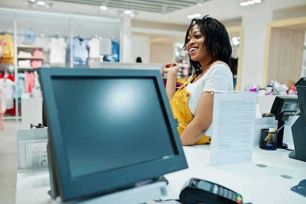 Happy african american woman customer with colored shopping bags paying near cash teminal