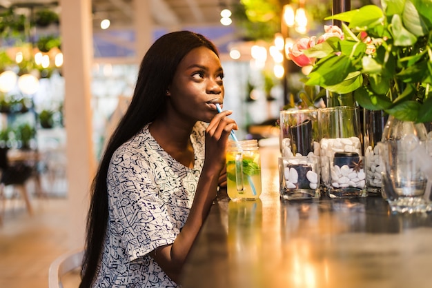 Happy African-American woman with glass of natural lemonade in cafe. Detox drink