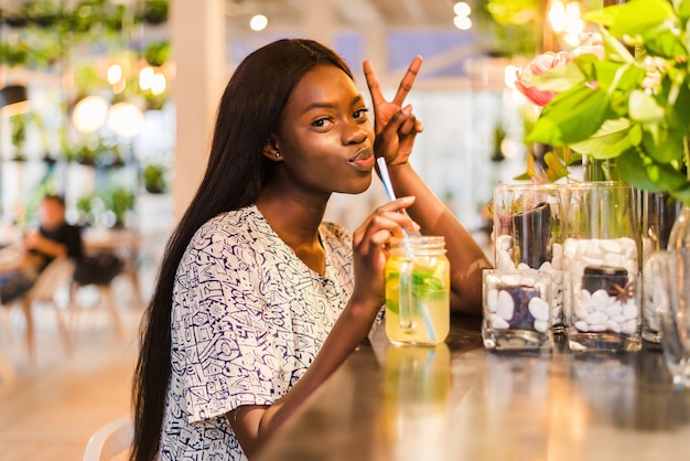 Happy African-American woman with glass of natural lemonade in cafe. Detox drink