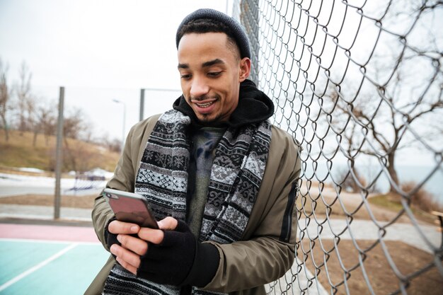 Счастливый афро-американский молодой человек, с помощью мобильного телефона на открытом воздухе