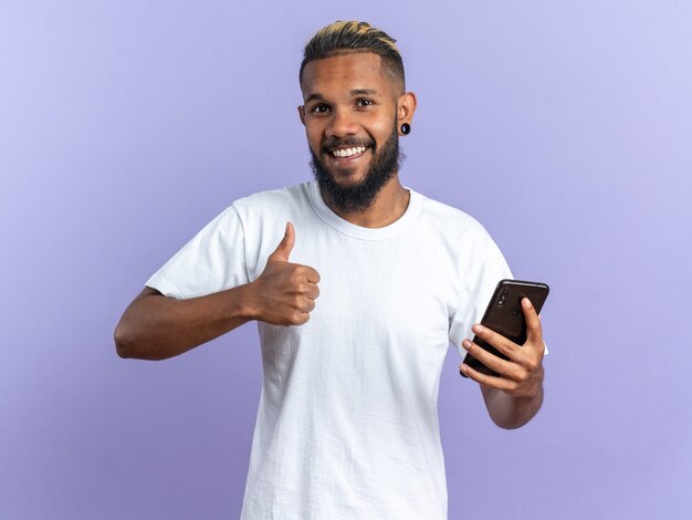 スマートフォンを保持している白いTシャツで幸せなアフリカ系アメリカ人の若い男
