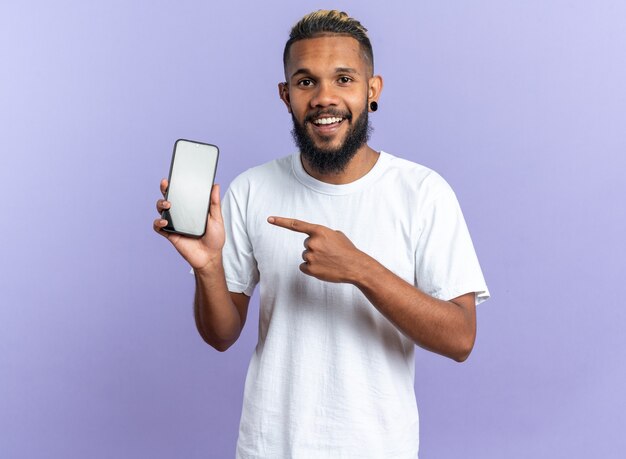 Happy african american young man in white t-shirt showing smartphone pointing