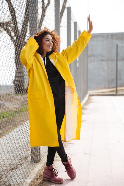 Happy african curly young lady walking and waving.