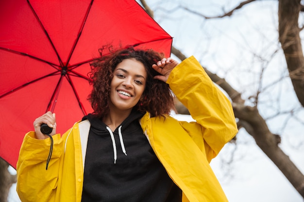 Free photo happy african curly young lady wearing yellow coat holding umbrella