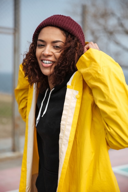 Happy african curly young lady wearing yellow coat walking outdoors