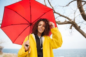Free photo happy african curly young lady wearing yellow coat with umbrella.