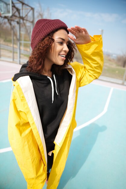 Happy african curly young woman wearing yellow coat walking