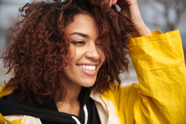 Foto gratuita giovane donna riccia africana felice che porta cappotto giallo