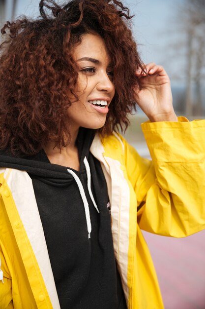 Happy african curly young woman wearing yellow coat