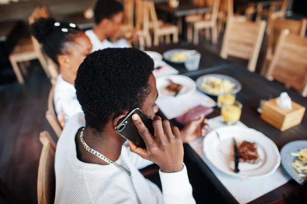 Счастливые африканские друзья сидят в чате в кафе и едят еду Группа чернокожих встречается в ресторане и ужинает