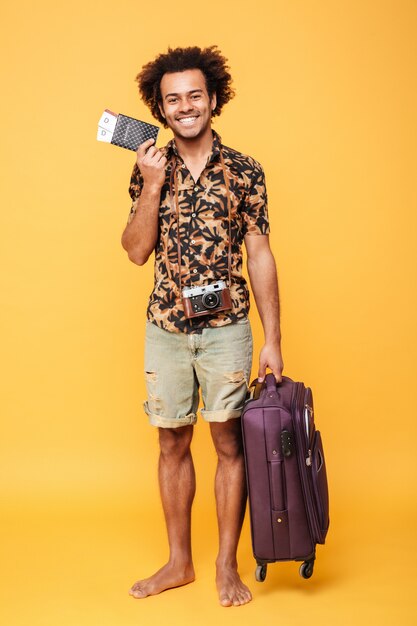 Счастливый африканский человек, держащий паспорт и чемодан.
