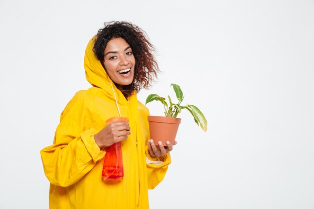 植物を保持しているレインコートで幸せなアフリカの女