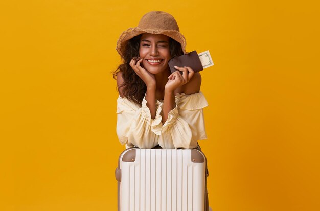 Happy african woman sitting with suitcase isolated on yellow background