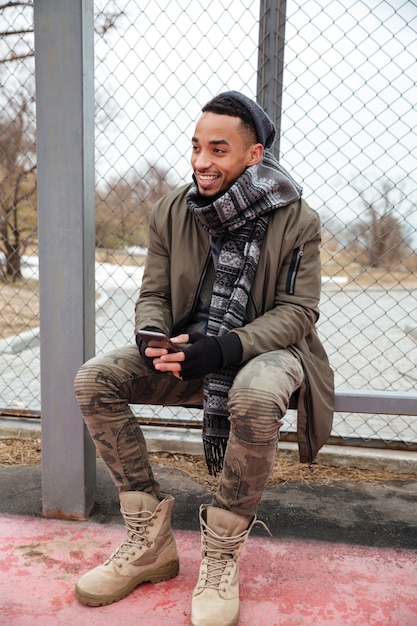 Free photo happy african young man using cell phone outdoors in autumn