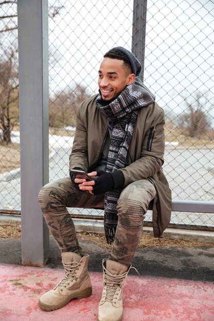 Happy african young man using cell phone outdoors in autumn