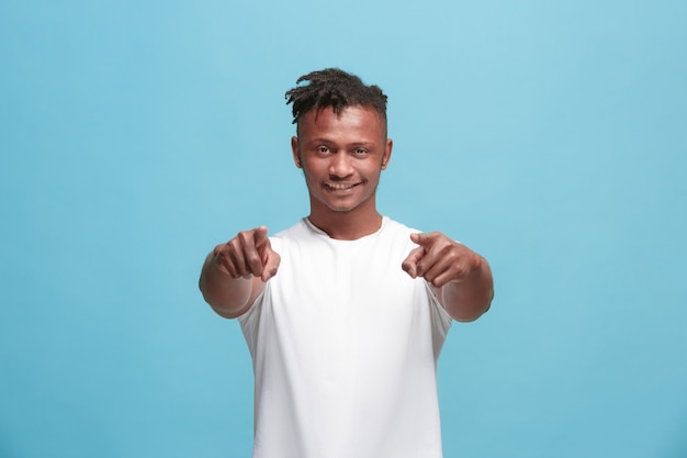 The happy afro-american businessman point you and want you, half length closeup portrait on blue background.