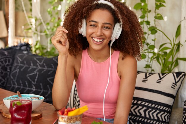 Happy Afro American female meloman listens music with high volume in headphones