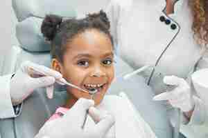 Foto gratuita bambino afro felice durante il controllo regolare dei denti in clinica dentale