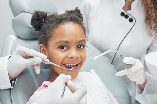 Happy afro kid on regular check up of teeth in dental clinic