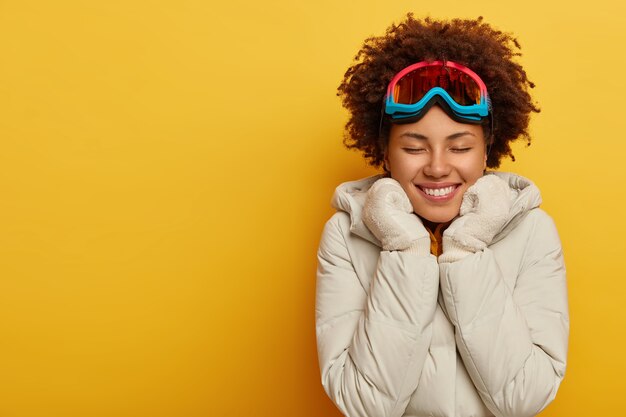 행복한 아프리카 여성은 스키 마스크, 따뜻한 니트 장갑 및 코트를 착용하고 야외 활동을 즐깁니다. 스노우 보드 착용에 기쁜 여성