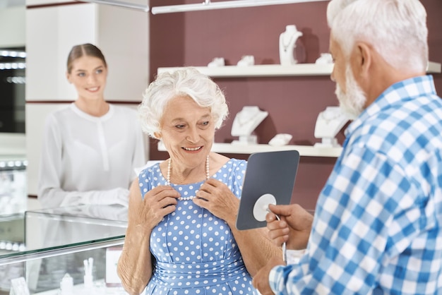 Счастливая пожилая женщина выбирает роскошное жемчужное ожерелье в магазине