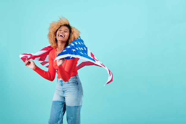 고립된 배경 위에 미국 국기가 서 있는 행복하고 흥분된 아프리카 여성. 독립 기념일 축하 개념입니다.