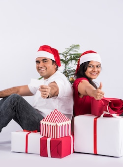 Счастливая и молодая индийская пара с рождественскими подарками, на белом фоне