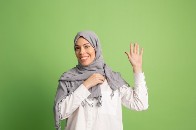 Hijab에서 행복 한 아랍 여자입니다. 녹색 스튜디오 배경에서 포즈 웃는 소녀의 초상화.